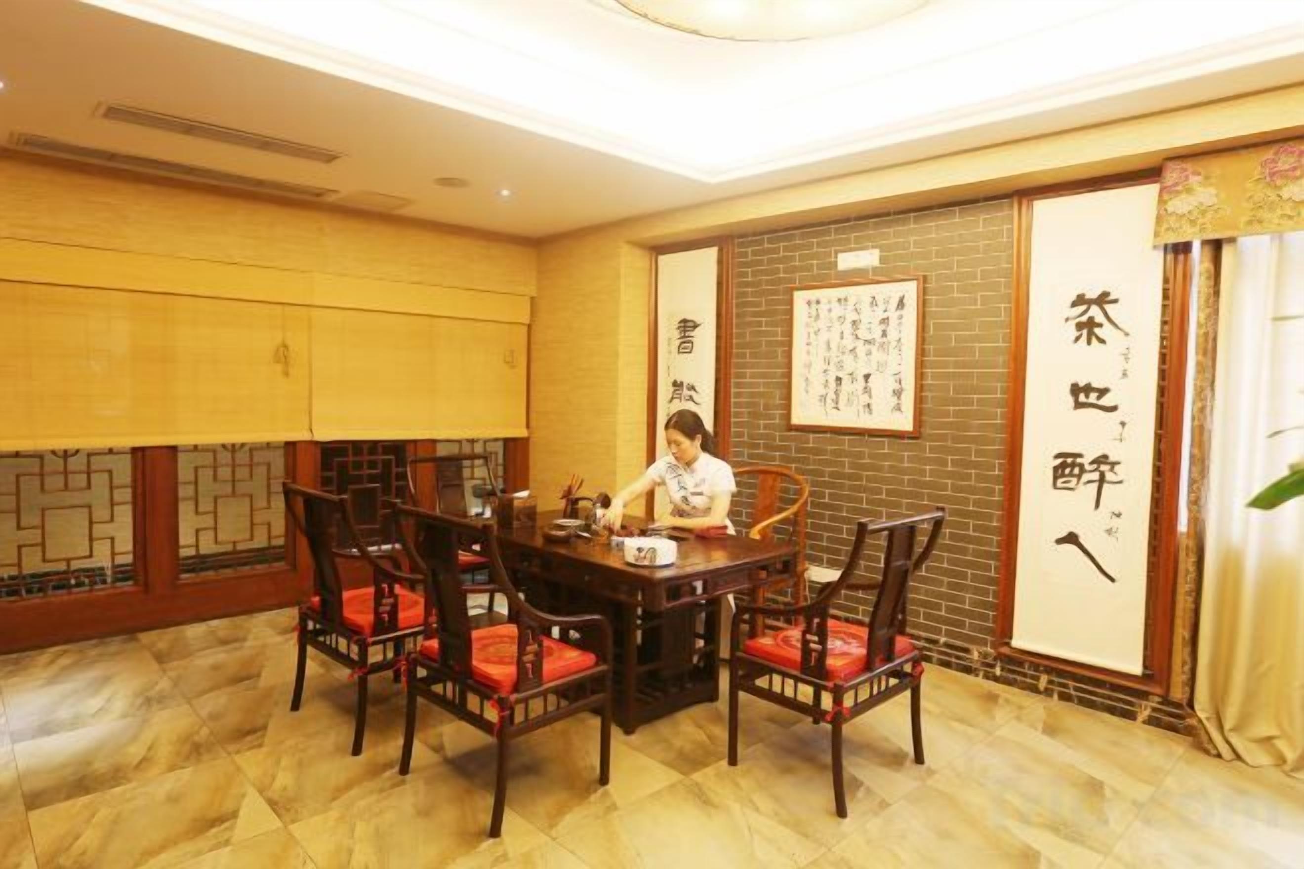 A traditional room with a wooden table and chairs, a person seated, and Chinese calligraphy on the wall.