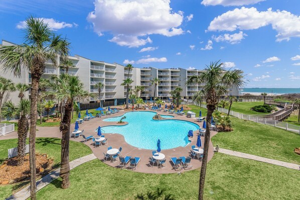 Un hôtel doté d’une grande piscine entourée de palmiers et de chaises longues, offrant une vue sur l’océan.