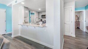Una cocina moderna con armarios blancos, encimera de granito y microondas de acero inoxidable.