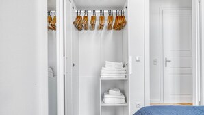 Un armario vestidor blanco con perchas de madera, repisas con toallas blancas dobladas y una puerta cerrada.