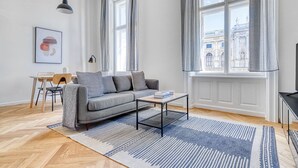 Una sala de estar moderna con un sofá gris, una mesa de centro y vistas a un edificio histórico a través de amplios ventanales.