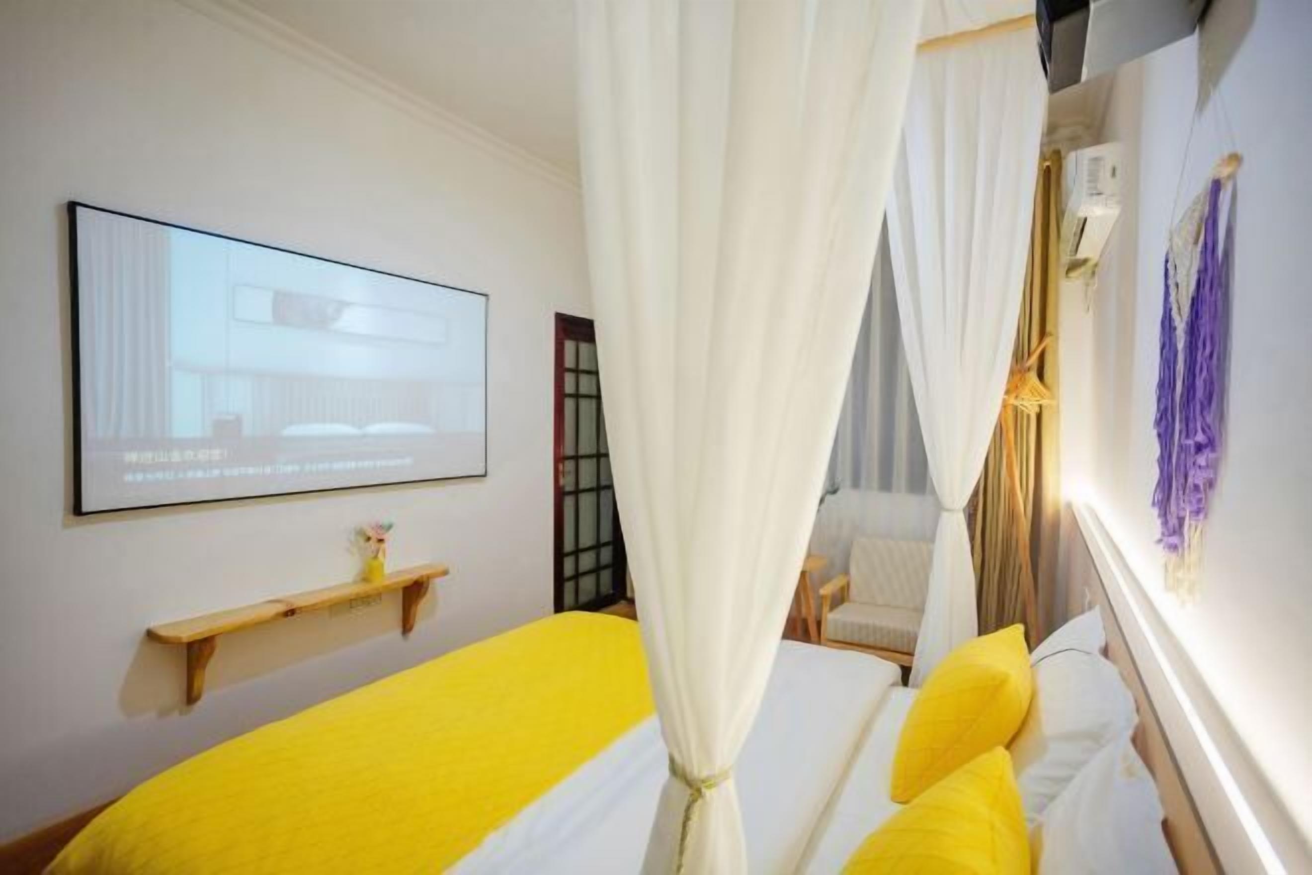 Un dormitorio con una cama, una cortina blanca, un televisor montado en la pared y un estante.