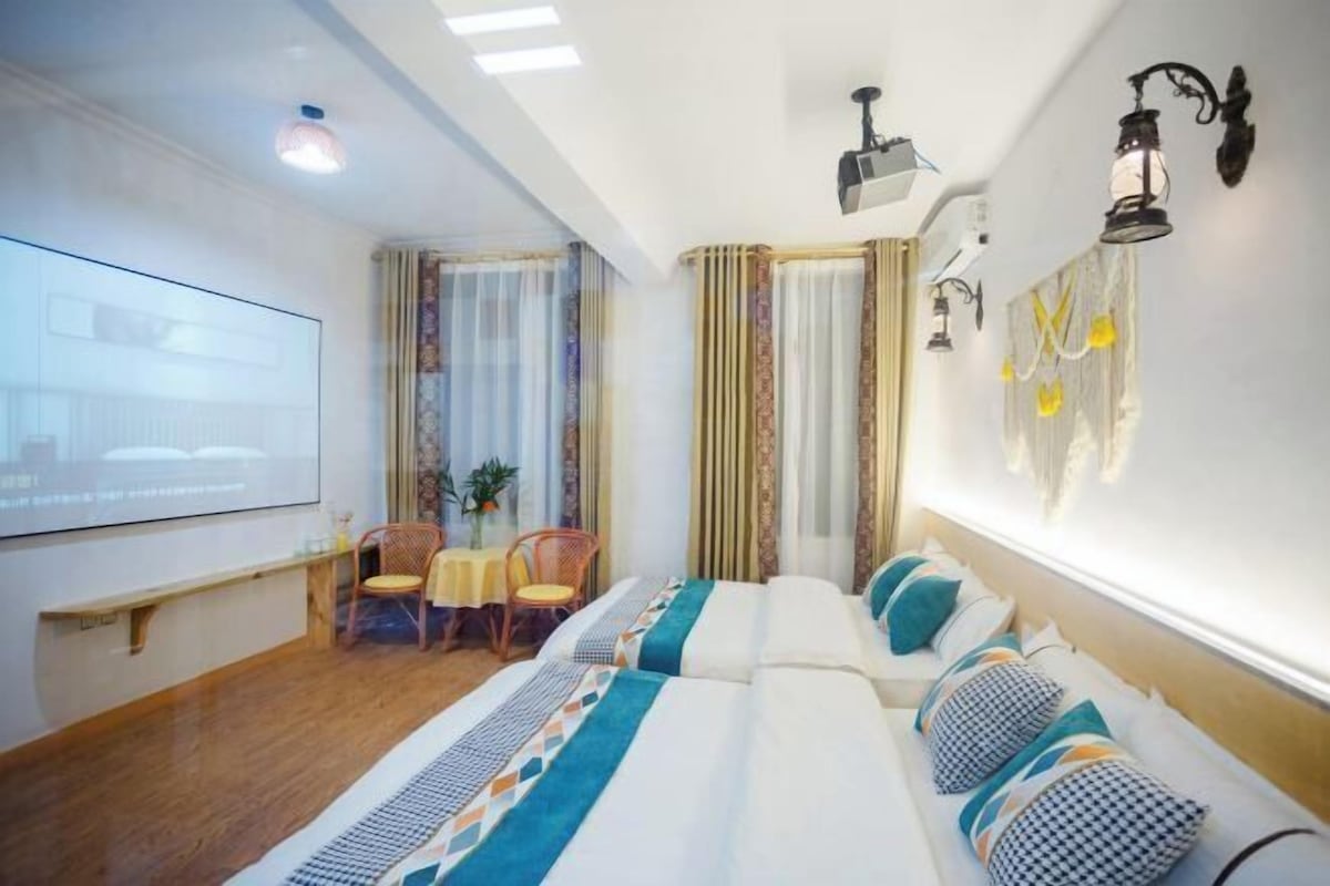 Hotellihuone, jossa on sänky, työpöytä tuolilla, projektorikangas ja ikkuna, jossa on verhot.