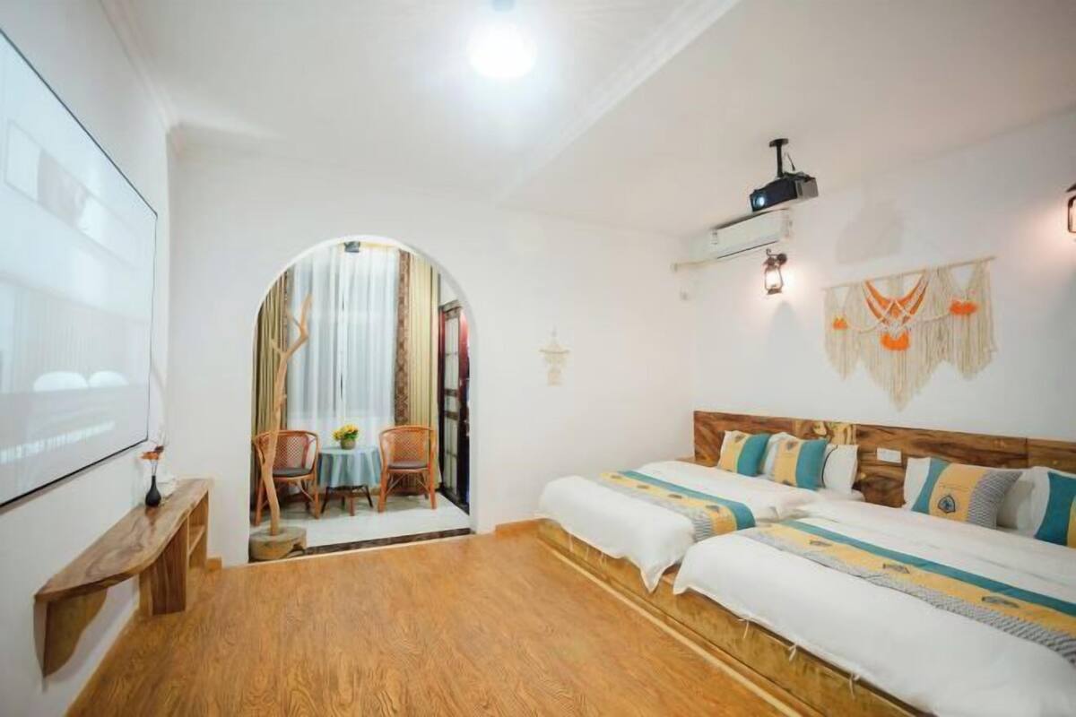 A room with two beds, a projector, a small table, and a view through an archway to another room.