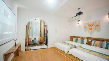 Una habitación con dos camas, un proyector, una mesita y vistas a otra habitación por medio de un arco.