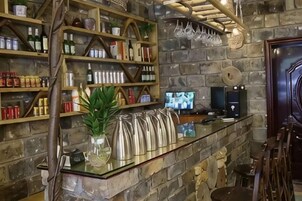 Zona de bar con estantes llenos de botellas, un mostrador de vidrio y una pared de piedra.