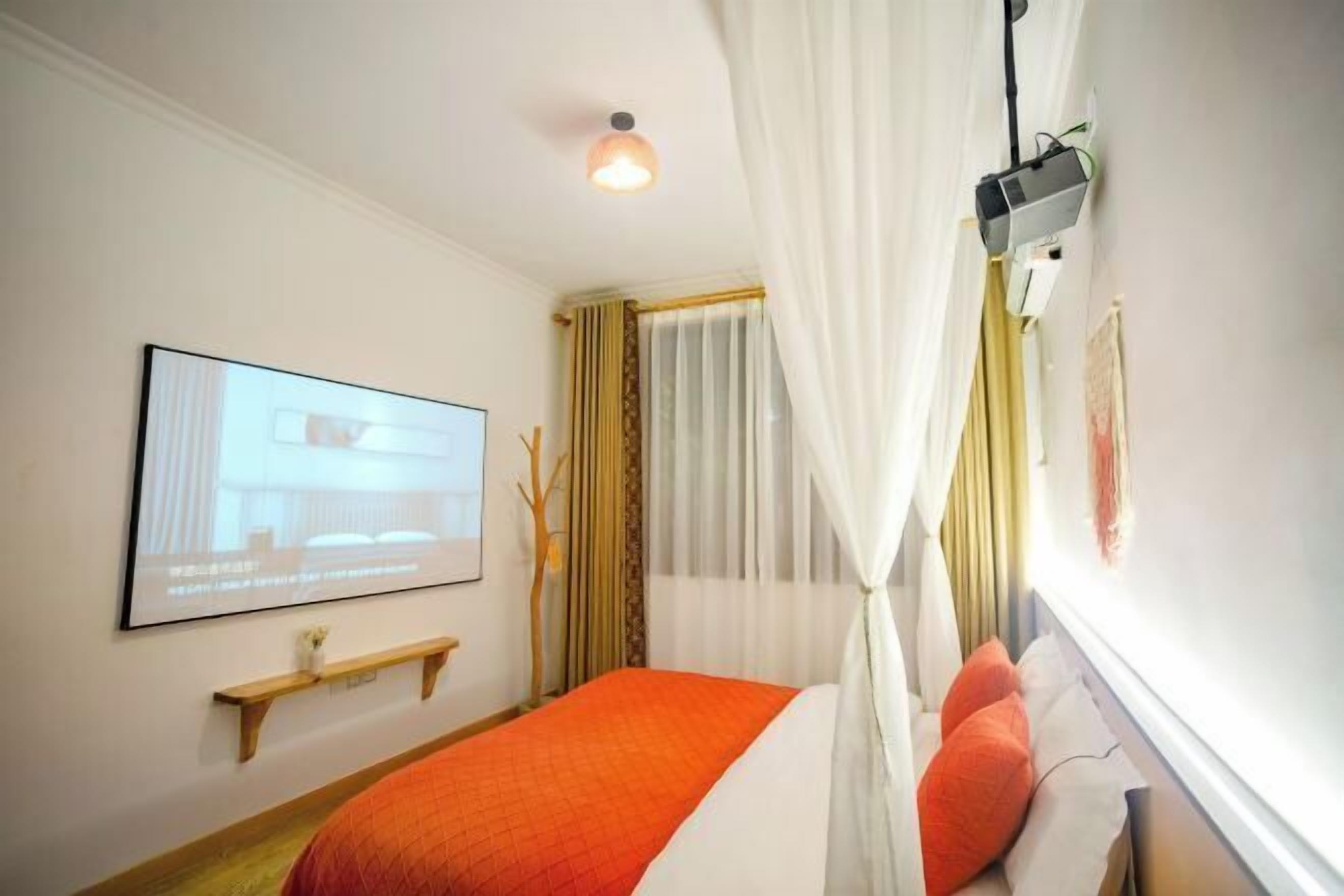 Una camera d'albergo con un letto, una TV a parete, uno scaffale e una finestra con tende.