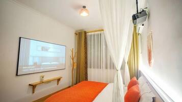 Una camera d'albergo con un letto, una TV a parete, uno scaffale e una finestra con tende.