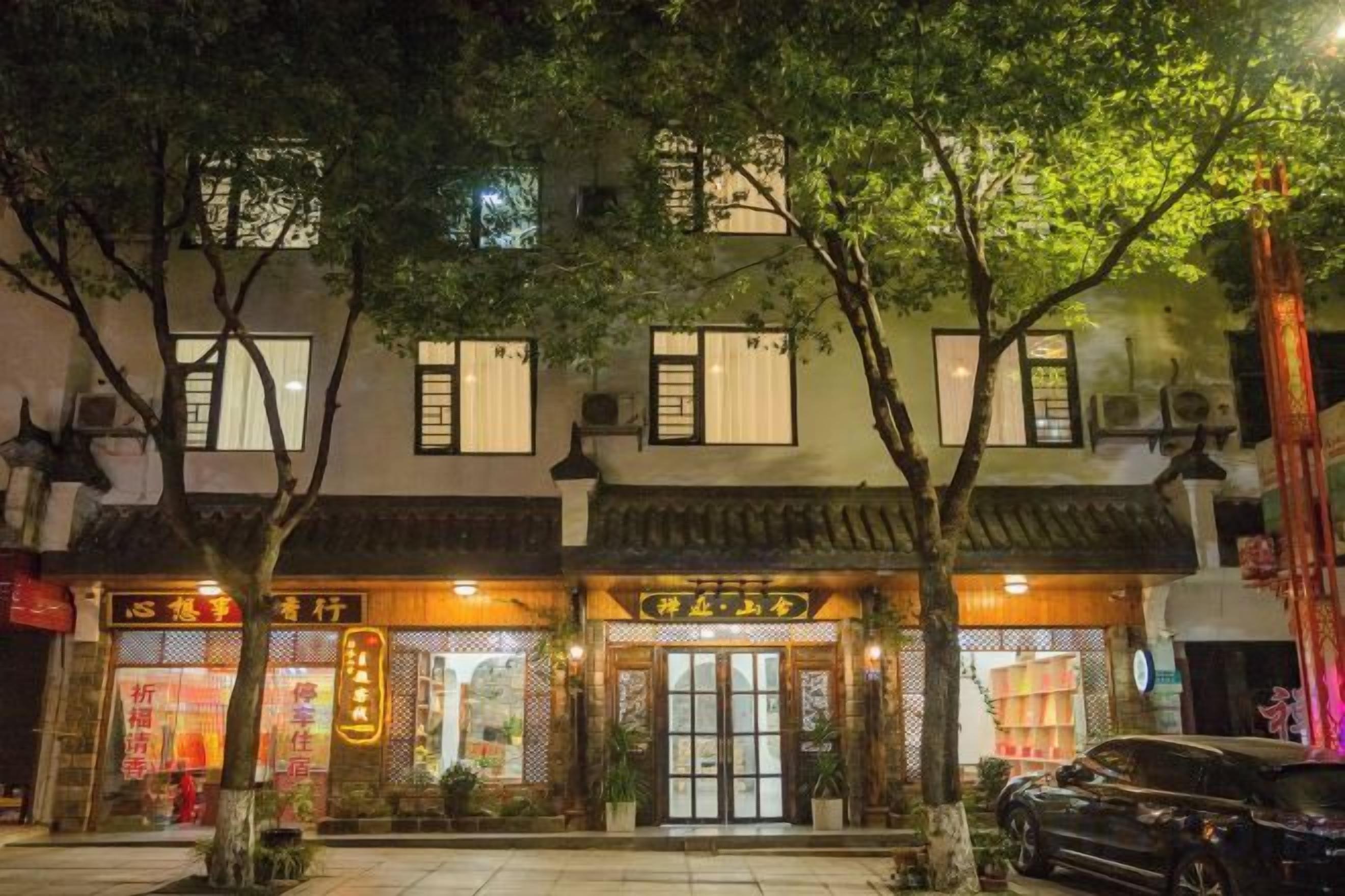 A traditional building with multiple storefronts, a car parked in front, and trees lining the sidewalk.