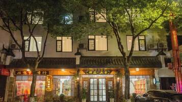 A traditional building with multiple storefronts, a car parked in front, and trees lining the sidewalk.