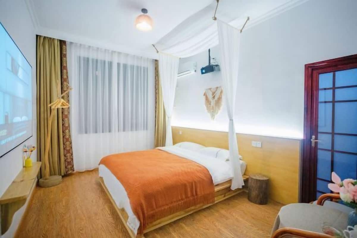 A hotel room with a bed, a TV, a wooden floor, a curtain, and a window.
