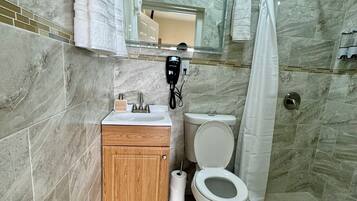 A bathroom with a marble wall, a wooden cabinet, a toilet, a shower area, and a mirror.