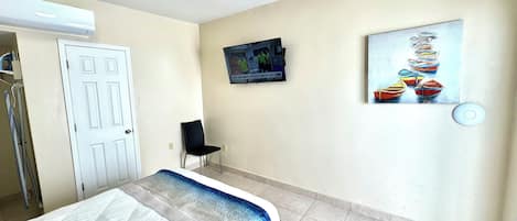A hotel room with a bed, a TV mounted on the wall, and a painting of boats.