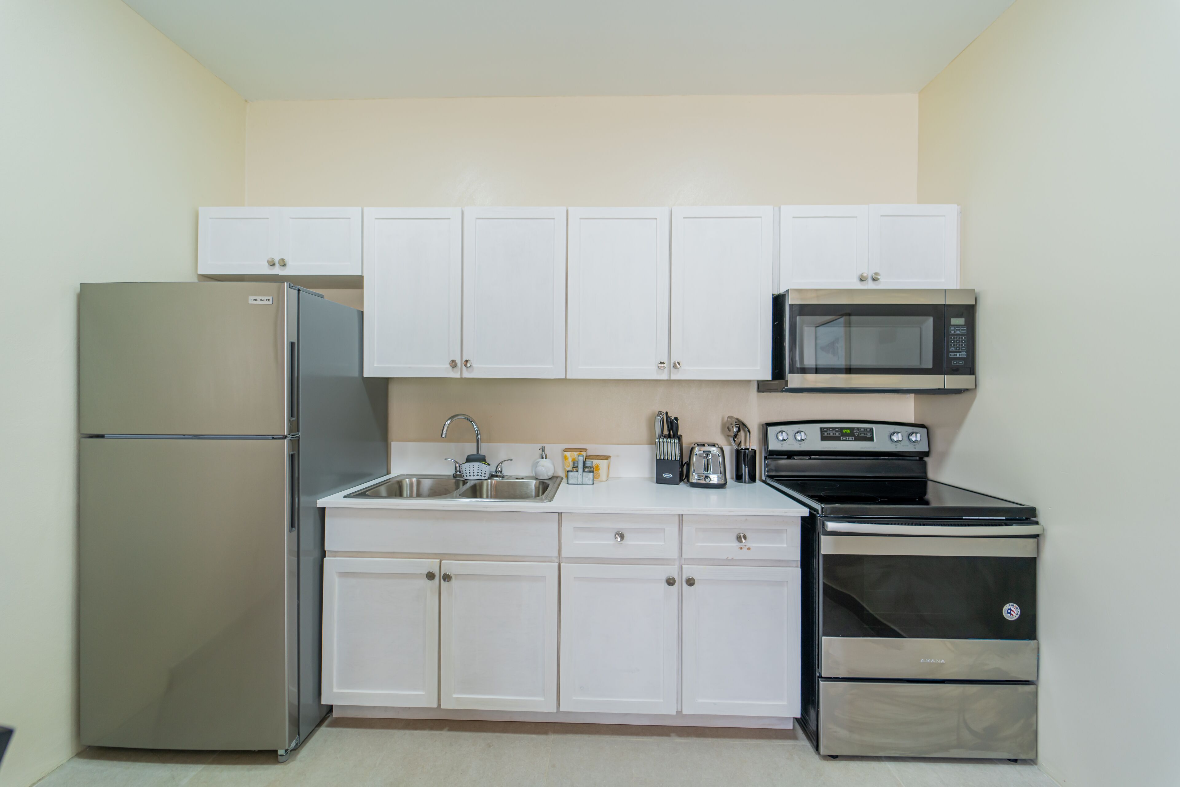 A compact kitchen with white cabinets, a stainless steel refrigerator, a microwave, and a stove.