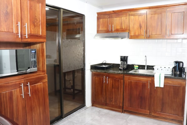Una cocina con armarios de madera, microondas, cafetera y lavamanos.