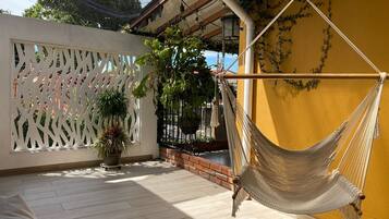 A hammock hanging on a yellow wall, a white lattice partition, and potted plants on a patio.