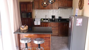 Cocina compacta con armarios de madera, encimera negra, dos taburetes de bar, refrigerador de acero inoxidable y microondas.
