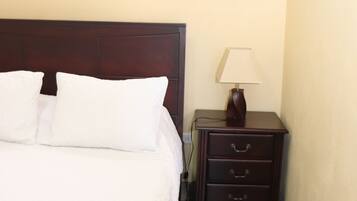 A hotel room with a bed, a nightstand with a lamp, an air conditioner, and a window.
