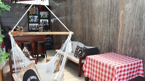Un espacio al aire libre acogedor con una hamaca, una mesa a cuadros y una barra con una variedad de botellas.