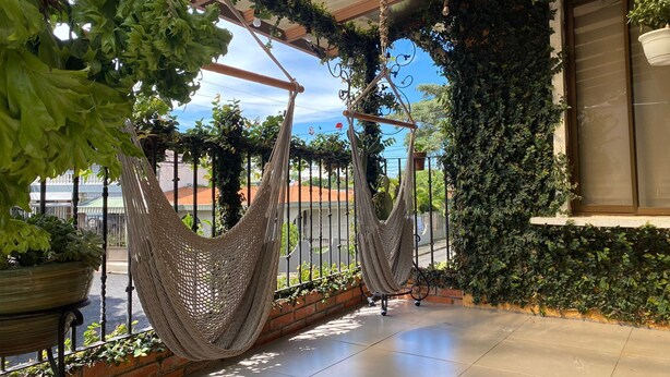 Una hamaca colgante con estructura metálica y mosquitera, frente a un fondo de vegetación y cielo despejado.