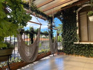 Una hamaca colgante con estructura metálica y mosquitera, frente a un fondo de vegetación y cielo despejado.
