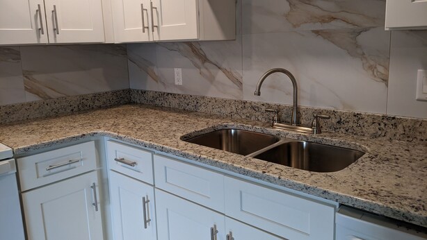 Una cocina con armarios blancos, encimera de granito y pileta de acero inoxidable.