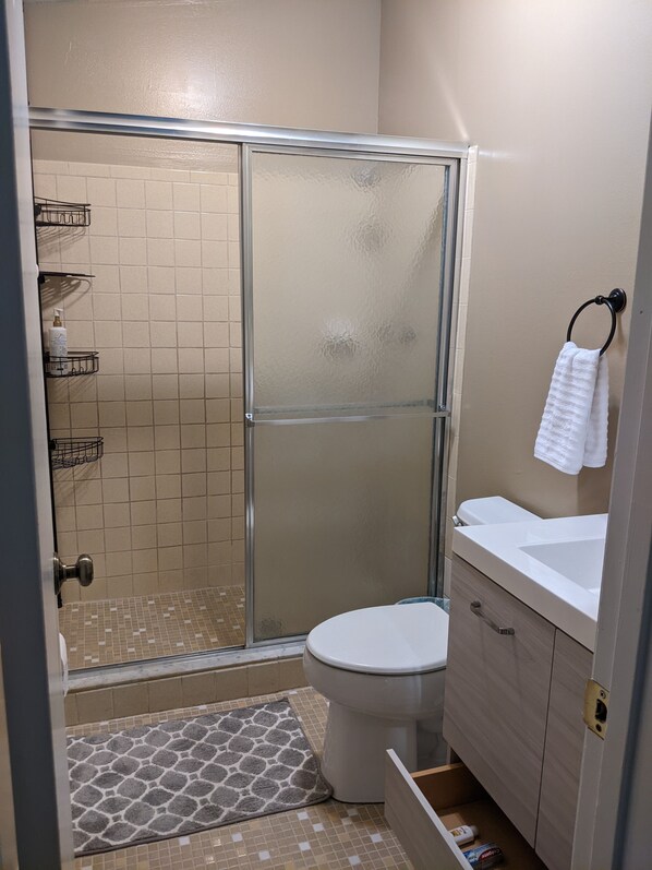 A bathroom with a glass shower enclosure, a toilet, a sink with a towel rack, and a small storage cabinet.