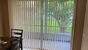 Un comedor con una mesa, sillas, una lámpara en el techo y vistas a un balcón a través de persianas verticales.