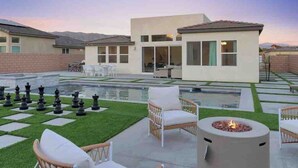 A modern outdoor patio with a chessboard, lounge chairs, and a fire pit. - Summer specials! Pool+spa+gameroom+putting green (Desert Hot Springs)