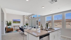 A modern kitchen with a large island, dining area, and a view of the desert. - Summer specials! Pool+spa+gameroom+putting green (Desert Hot Springs)
