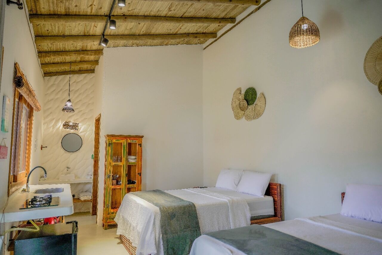 Quarto com duas camas, um armário de madeira, um espelho redondo e uma luminária suspensa.