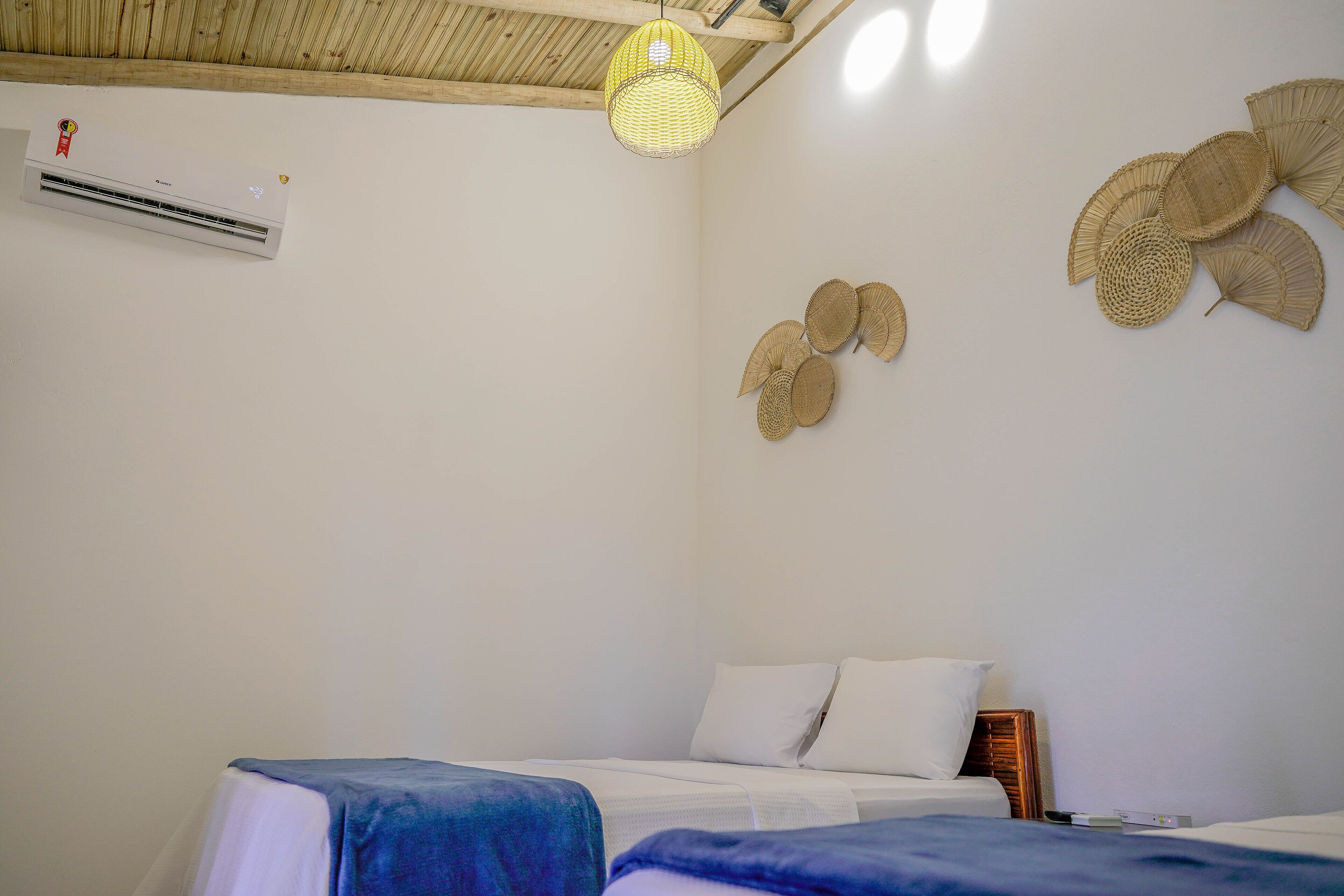 A bedroom with a bed, an air conditioner, a hanging light fixture, and woven wall decorations.