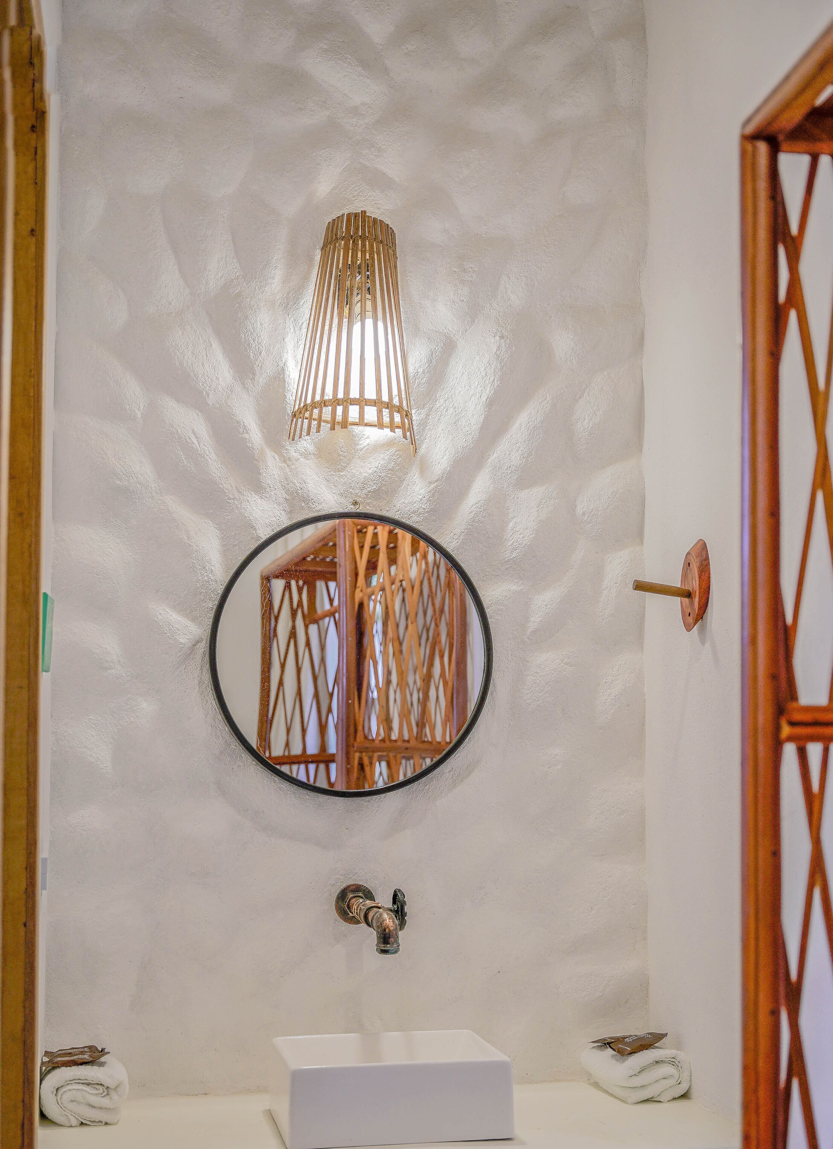 Un baño con un lavamanos blanco, un espejo redondo y una lámpara de pared.