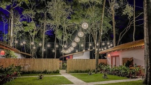 A garden pathway leading to a building with a tiled roof, surrounded by trees and a bamboo fence.