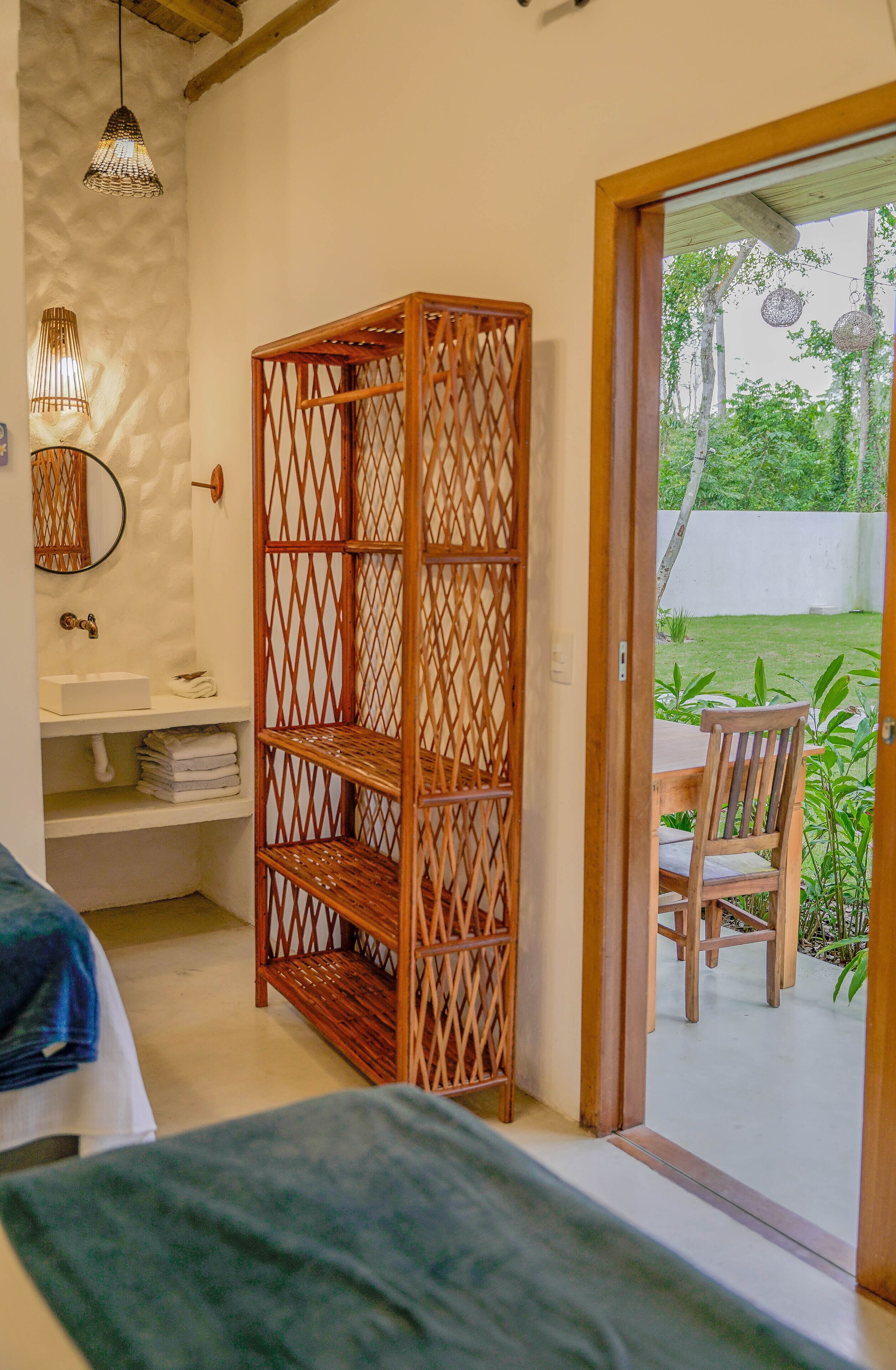 Une chambre avec une étagère en bois, une table de chevet, un miroir et une vue sur une terrasse extérieure avec une table et des chaises.