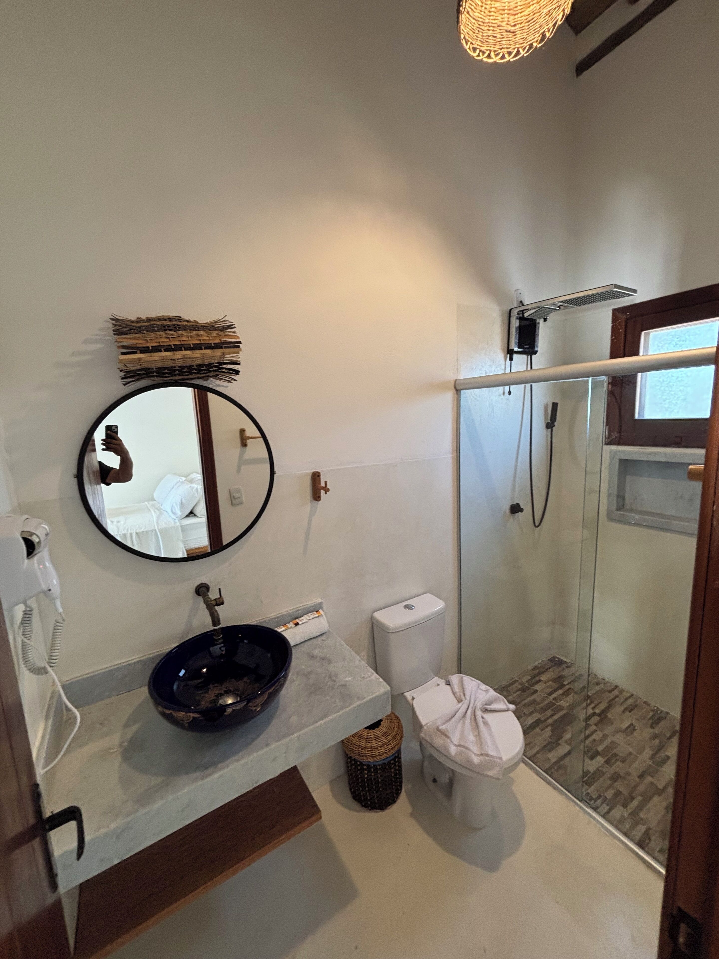 Ein Badezimmer mit rundem Spiegel, Waschbecken, Toilette und einer Duschkabine.
