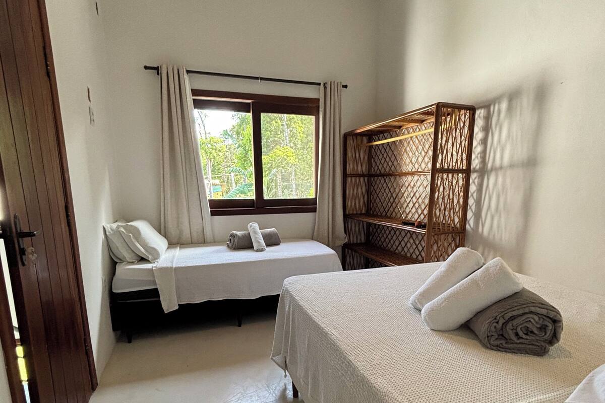 A bedroom with two beds, a window with curtains, a wooden headboard, and a ceiling fan.