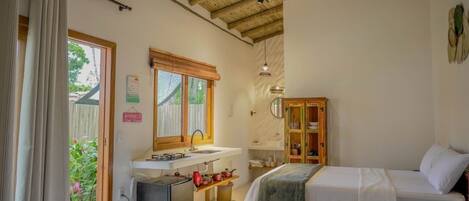 A bedroom with two beds, a wooden ceiling, a sink, and a window with a view of greenery.