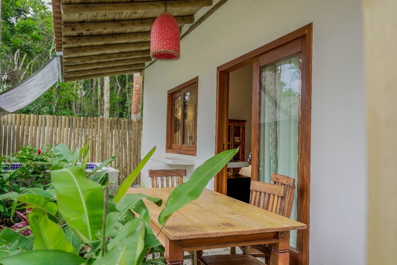 Een houten tafel en stoelen onder een houten pergola, met een rode hanglamp.