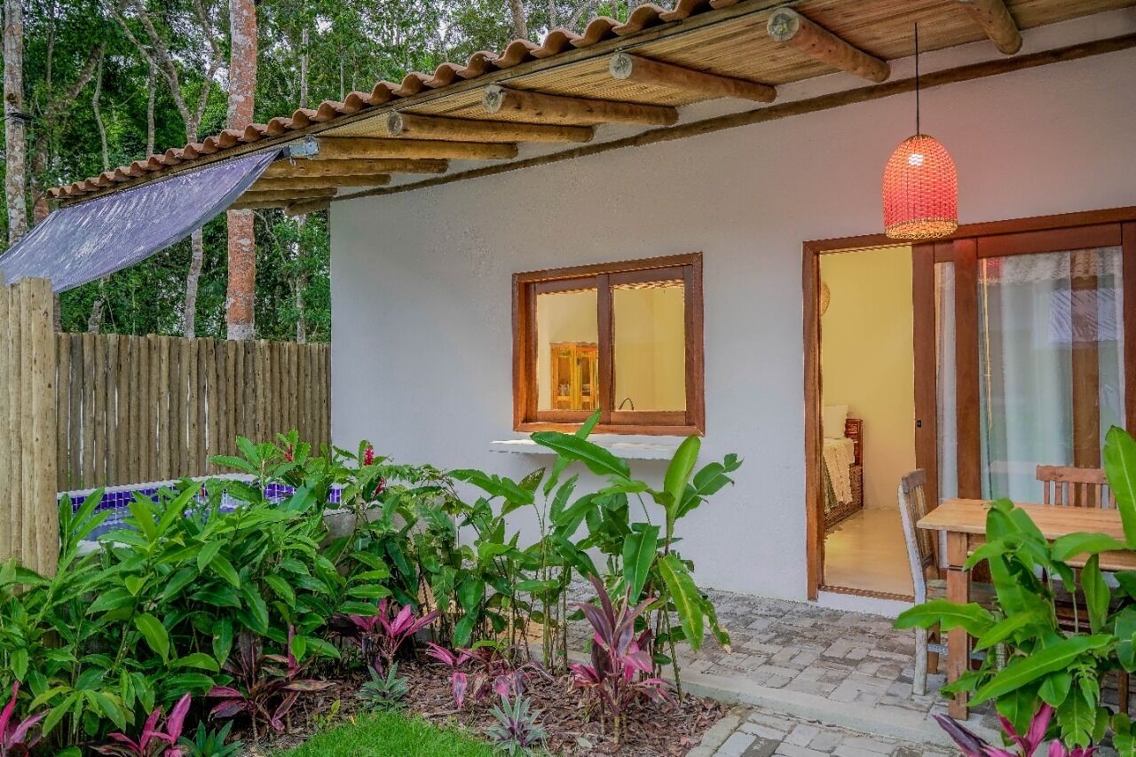 Una casa con una pergola in legno, una finestra e un portone che dà su una stanza con tavolo e sedie.