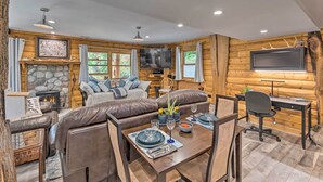 Ein gemütliches Blockhaus-Interieur mit Kamin aus Stein, Ledersofa, Esstisch und einem an der Wand montierten Fernseher.
