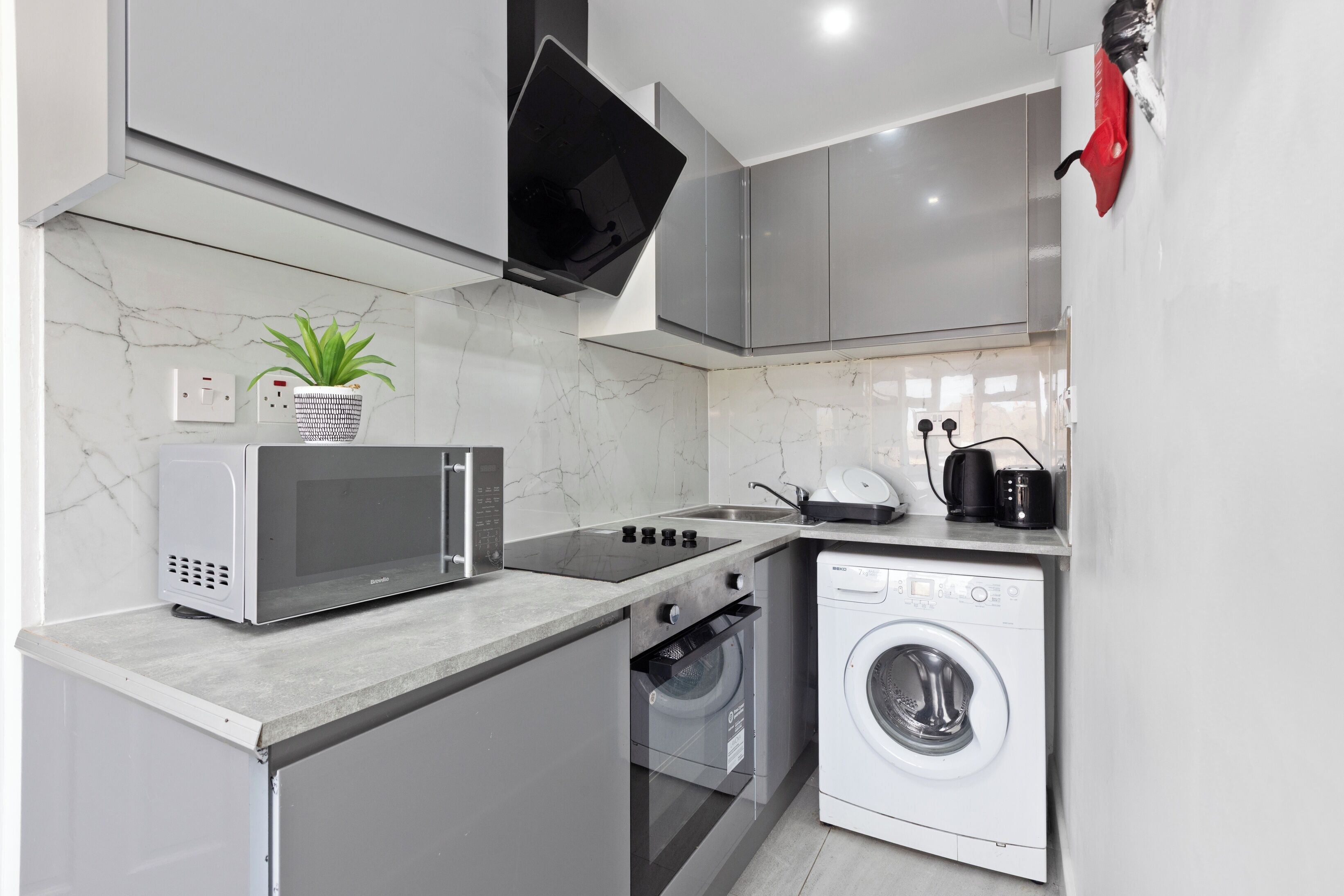 Cocina compacta equipada con microondas, estufa, lavadora y una pequeña planta.