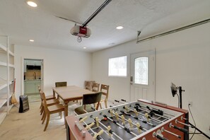 Ett rum med ett fotbollsspel, ett matbord, stolar, ett köksområde och en projektor i taket.