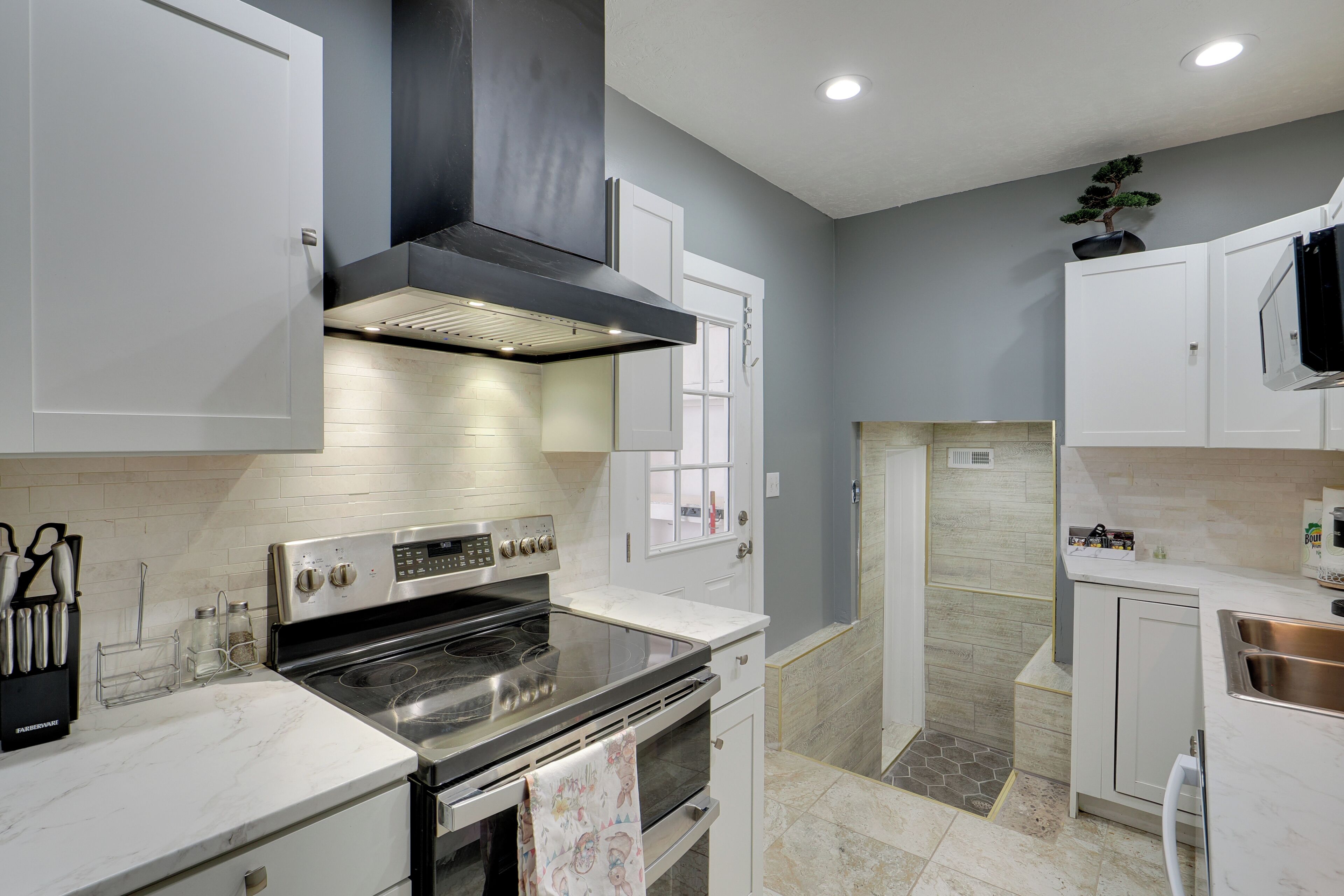 A modern kitchen with white cabinets, stainless steel appliances, and a black range hood.