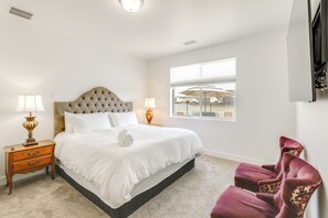 Una camera da letto ordinata con un letto grande, due lampade da comodino, un comodino in legno, una poltrona confortevole e una finestra con vista sugli edifici.