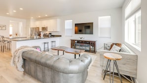 Uma sala de estar moderna com um sofá de couro cinza, uma mesa de centro de madeira e um banquinho.