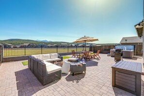 Una terrazza esterna con mobili in vimini, un barbecue e vista su un campo sportivo.