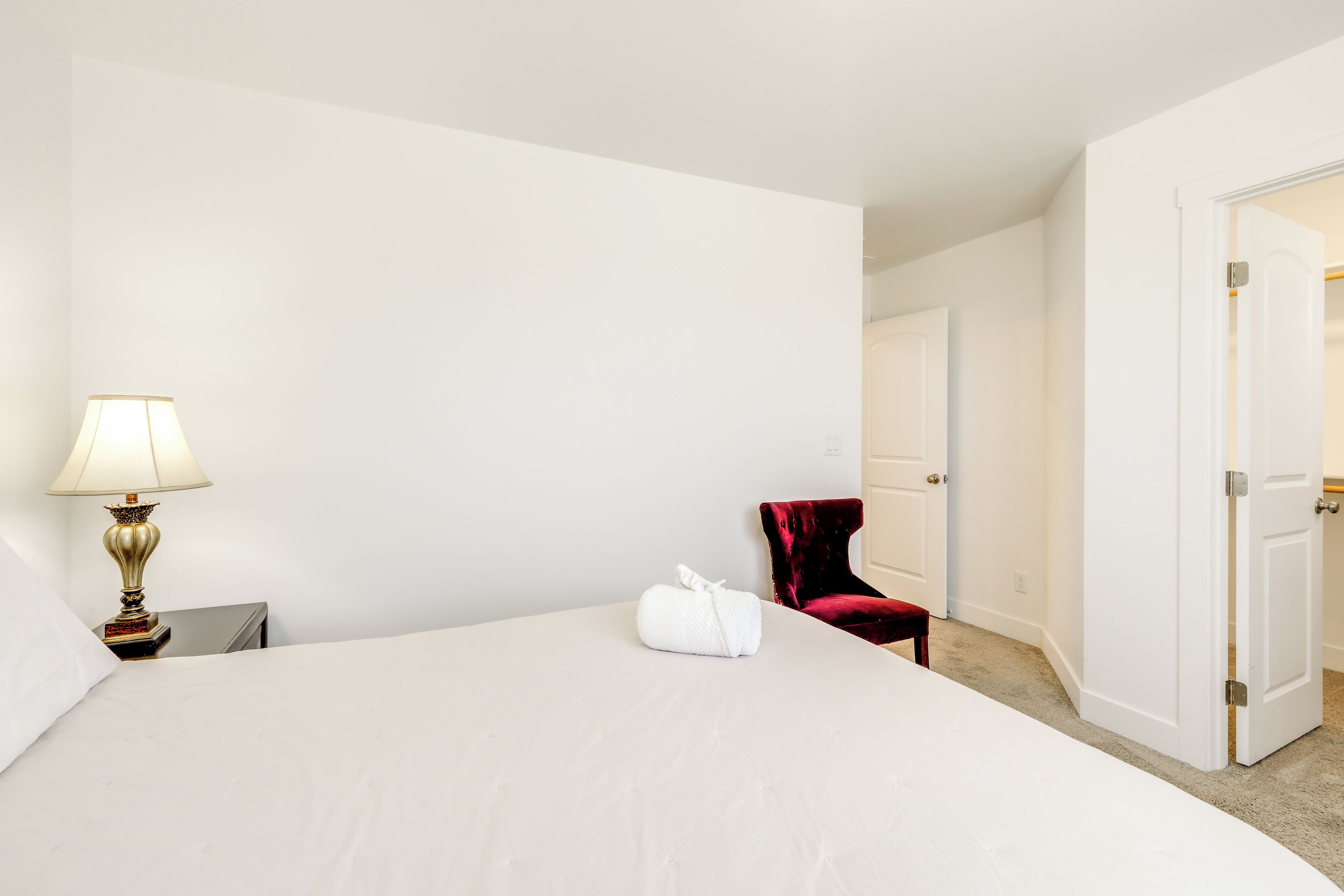 Una habitación de hotel con una cama, una lámpara, una silla roja y una puerta que da a otra habitación.
