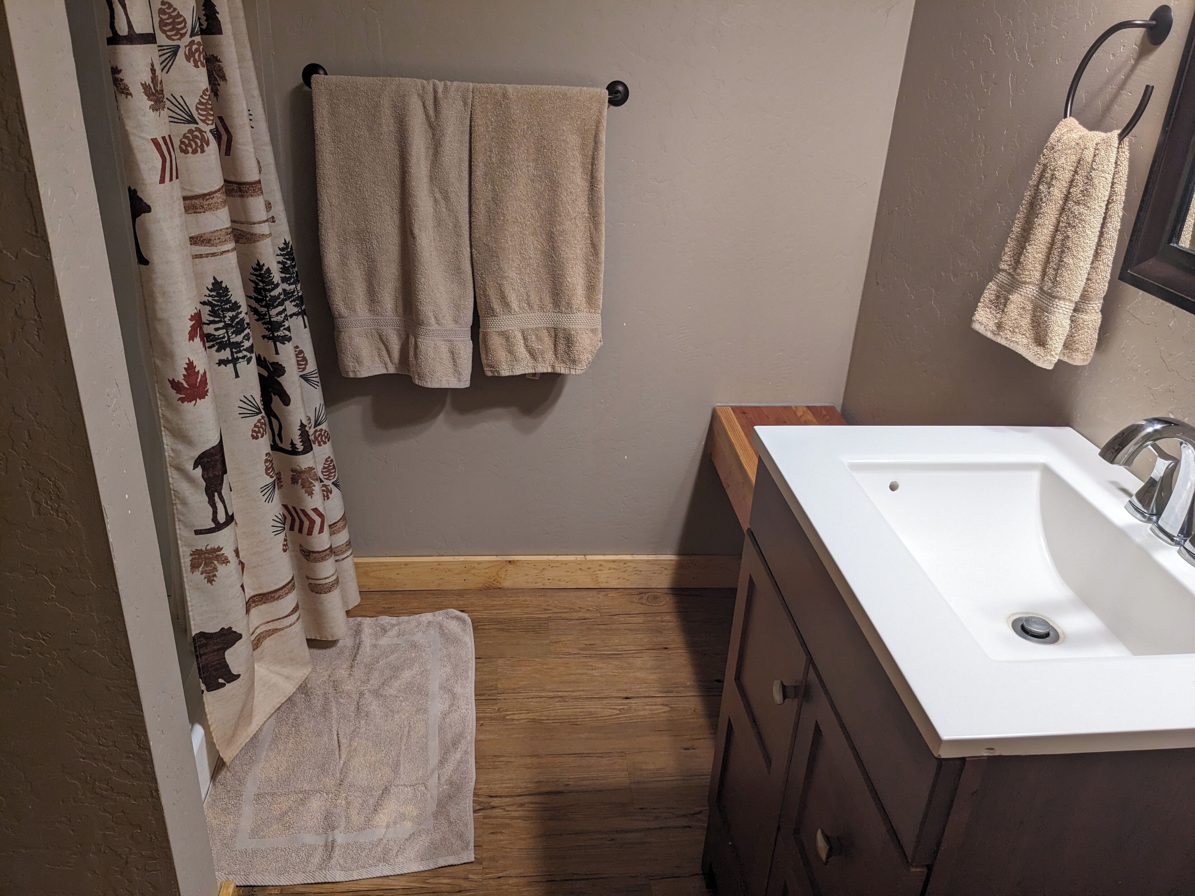 A bathroom with a wooden floor, a white sink, a mirror, and a towel rack with two towels.
