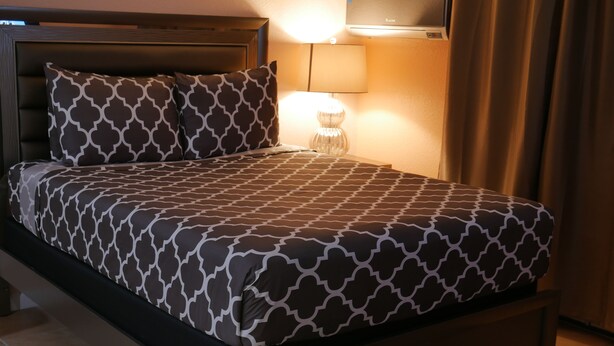 Een net opgemaakt bed met beddengoed met een patroon, een bedlamp en een wandairconditioner.